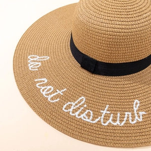 Detailed view of woven straw hat featuring 'do not disturb' embroidery and black ribbon