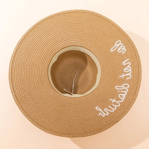 Close-up of khaki straw hat with white cursive embroidery and adjustable drawstring