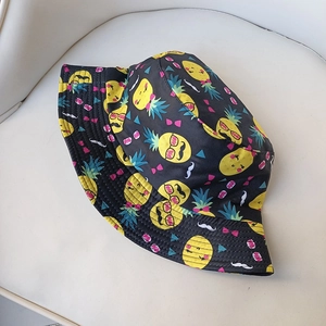 Detail of a black bucket hat with funny cartoon pineapple patterns on a beige base