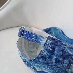 Detail of blue denim baseball cap featuring an adjustable gold buckle and fine stitching