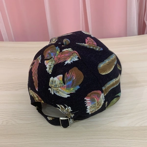 Detail view of adjustable metal buckle and colorful feather print on black cotton baseball cap