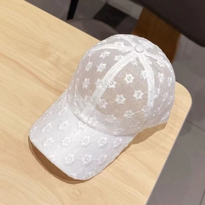 Berretto da baseball in pizzo bianco con ricami floreali posizionato su un tavolo di legno