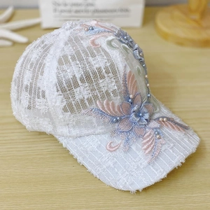 Detail view of white lace baseball cap with floral embroidery and pearl beads