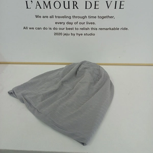 Detailed view of light gray slouchy beanie with fine horizontal knit texture on a white board