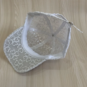 Detail of white lace mesh baseball cap featuring heart embroidery and adjustable back strap