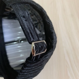 Close-up of black corduroy baseball cap with adjustable silver metal buckle at the back
