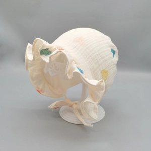 Detail einer Baby-Baumwollhaube mit bunten Herzen und Rüschensaum auf grauem Hintergrund
