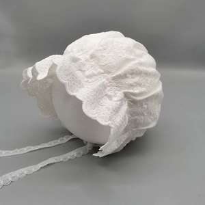 Close-up of white baby bonnet featuring intricate lace embroidery and ruffled sun brim