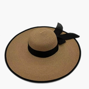 Detail of wide brim straw hat featuring black ribbon bow and elegant woven texture