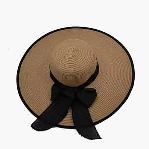 Women's wide brim straw sun hat with black bow and edge trim on white background