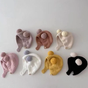 Detail view of plush baby earflap hats with pom-poms and wooden buttons in seven colors