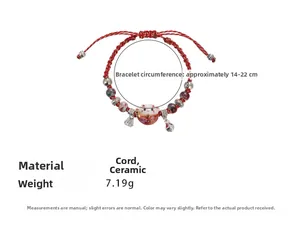 Detail of red handmade cord bracelet featuring a ceramic lucky cat and a silver fan charm