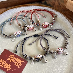 Detail of five colorful woven bracelets with ceramic lucky cat beads and metal bells