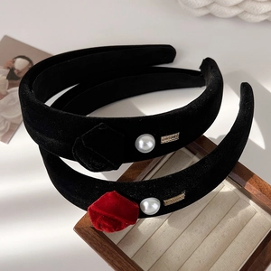 Elegant black velvet rose headband with pearls and gold accents on a wooden display