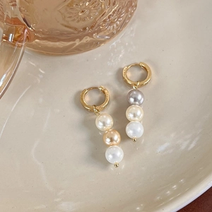 Détail de boucles d'oreilles créoles dorées avec perles en dégradé sur plateau en céramique