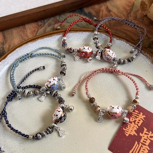 Detailed view of handmade ceramic Maneki Neko cat charm bracelets with adjustable braided cords