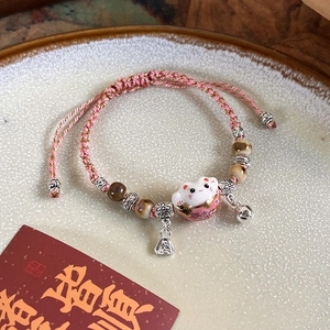 Macro detail of hand-painted ceramic Maneki Neko cat charm with a woven pink rope bracelet