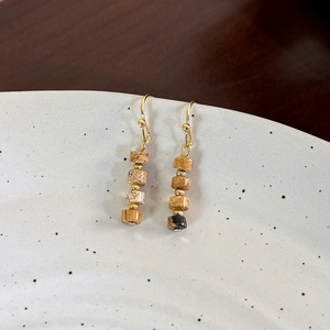 Macro detail of vintage tiger eye stone beaded earrings with golden hooks on ceramic tray