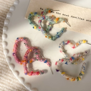 Gros plan de boucles d'oreilles cœur en laine arc-en-ciel à texture douce