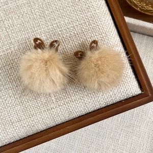 Detail view of cute beige plush rabbit ear hair clips on a natural linen display board