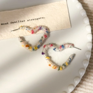 Gros plan de boucles d'oreilles cœur enveloppées de fil arc-en-ciel sur une assiette