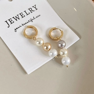 Gros plan de boucles d'oreilles dorées avec perles dégradées blanches et champagne