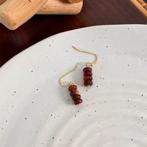Detailed view of vintage gold hook earrings with dark brown beads on ceramic plate