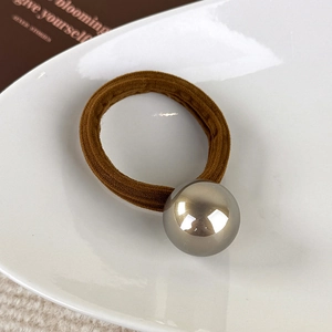 Gros plan d'un élastique à cheveux marron avec une grande perle métallique grise dans un plat