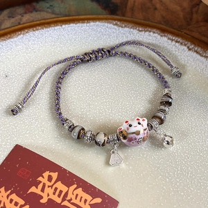 Detail of hand-woven purple bracelet with ceramic lucky cat and silver bell charm