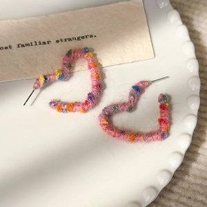 Détail de boucles d'oreilles cœur en laine arc-en-ciel avec textures tissées colorées