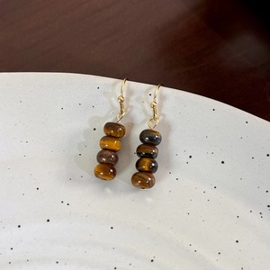 Close-up of vintage tiger eye stone beaded earrings with gold hooks on a ceramic dish