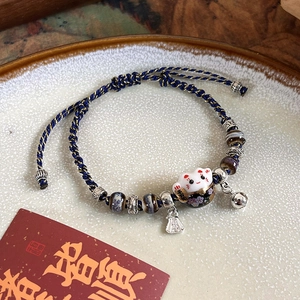 Macro shot of ceramic lucky cat charm with woven blue cord and metallic bell details