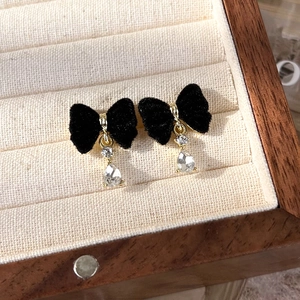 Close-up of black velvet bow earrings with golden metal and waterdrop glass pendant