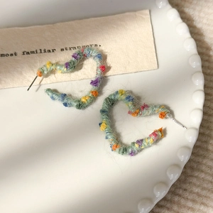 Détail de boucles d'oreilles cœur enveloppées de fil arc-en-ciel aux couleurs macaron