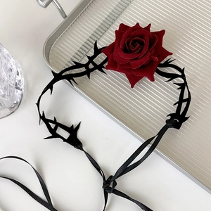 Close-up of gothic black thorn choker with a deep red velvet rose on silver tray