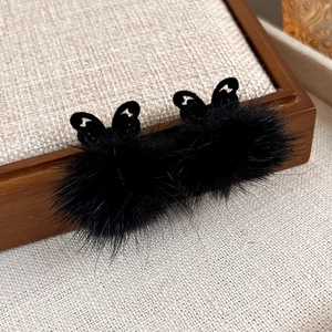 Detail of hollow butterfly earrings with soft black plush balls on a linen display tray