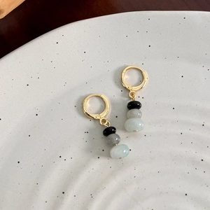 Detail of vintage gold hoops with black, gray and green beads on ceramic plate