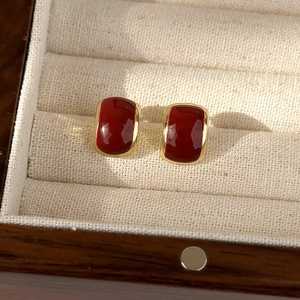 Detailed close-up of vintage dark red enamel earrings with gold edges in a wooden box