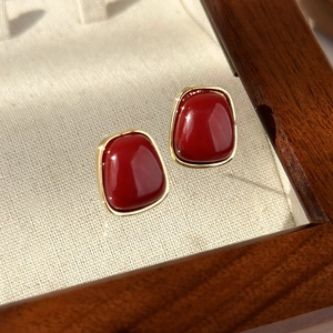Macro detail of vintage deep red enamel heart earrings with gold trim on wooden box