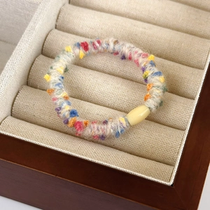 Close-up of a colorful knitted hair tie with plush texture and yellow resin fastener