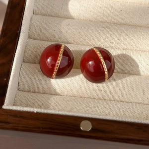 Macro shot of burgundy red ball stud earrings with gold bead belt in a velvet box