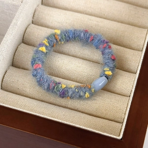Detailed close-up of grey-blue plush hair scrunchie with colorful wool accents in a box