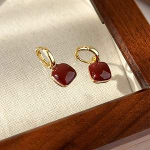 Macro detail of red enamel geometric heart earrings on a vintage canvas background