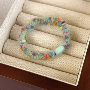 Detail of green knit hair scrunchie with colorful plush balls in a beige jewelry box