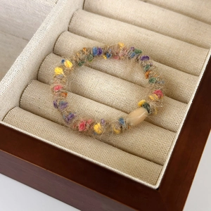 Close-up of beige plush hair tie with colorful felt balls in a wooden jewelry box