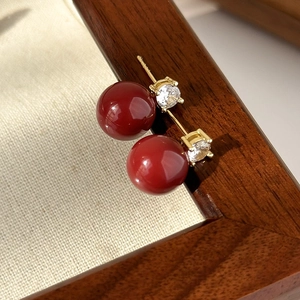 Close-up of vintage deep red bead and zircon stud earrings on a beige textured fabric