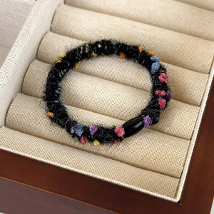 Detailed view of black fuzzy hair tie with colorful yarn dots on beige velvet box