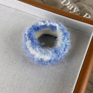 Détail d'un chouchou tricoté bleu ciel et blanc avec une texture pelucheuse douce