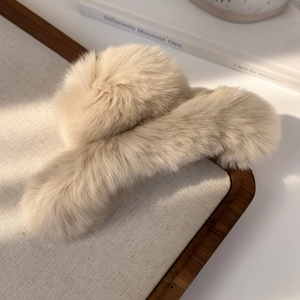 Detailed close-up of a large cream plush shark hair claw clip on a rustic linen backdrop