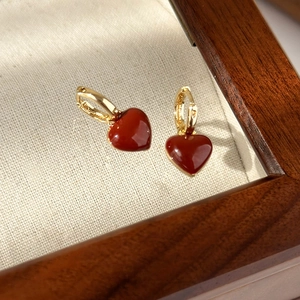 Close-up of retro gold hoop earrings with deep red heart charms on a wooden tray